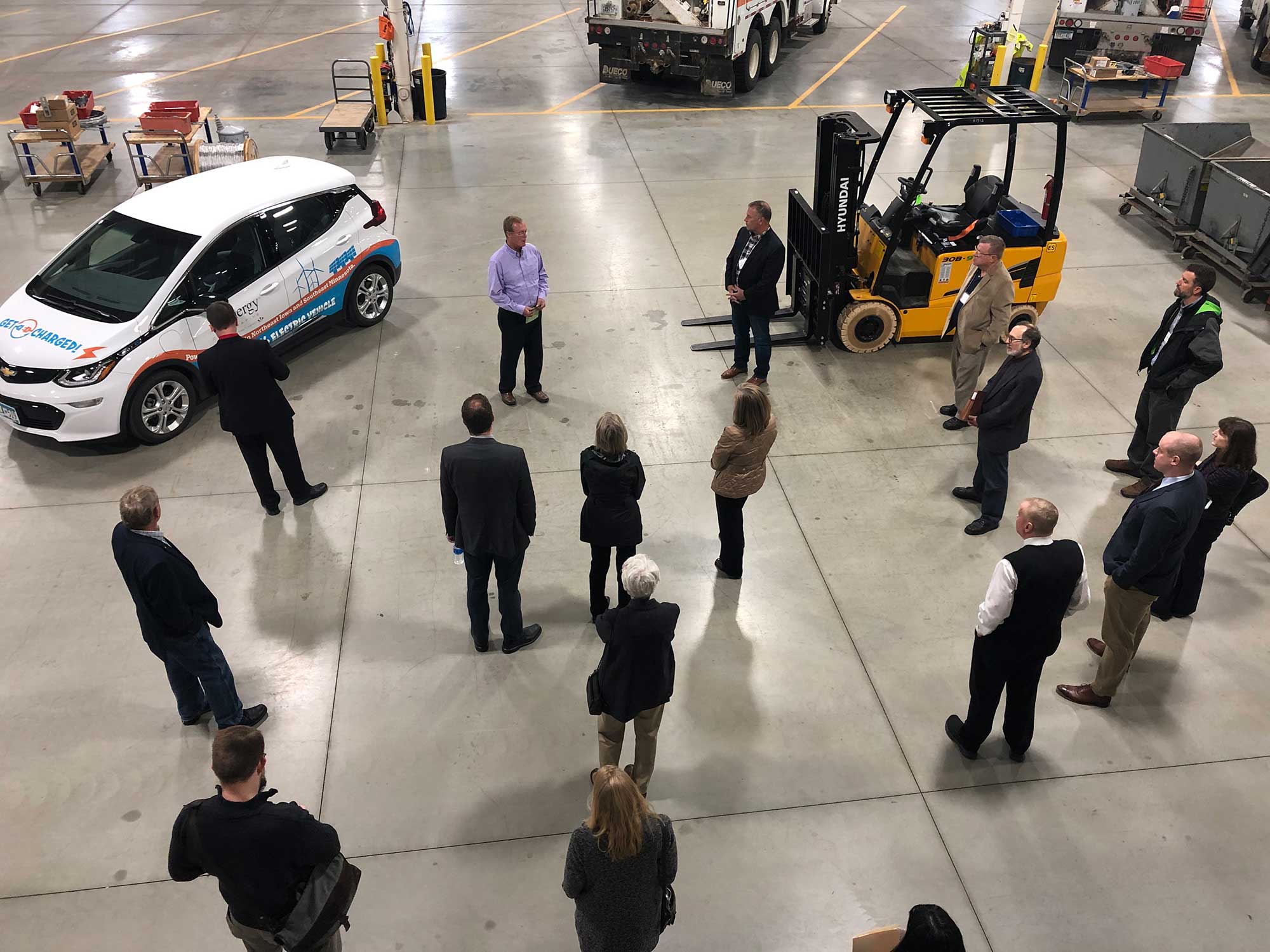 overhead shot of group of people standing near electric car and electric forklift